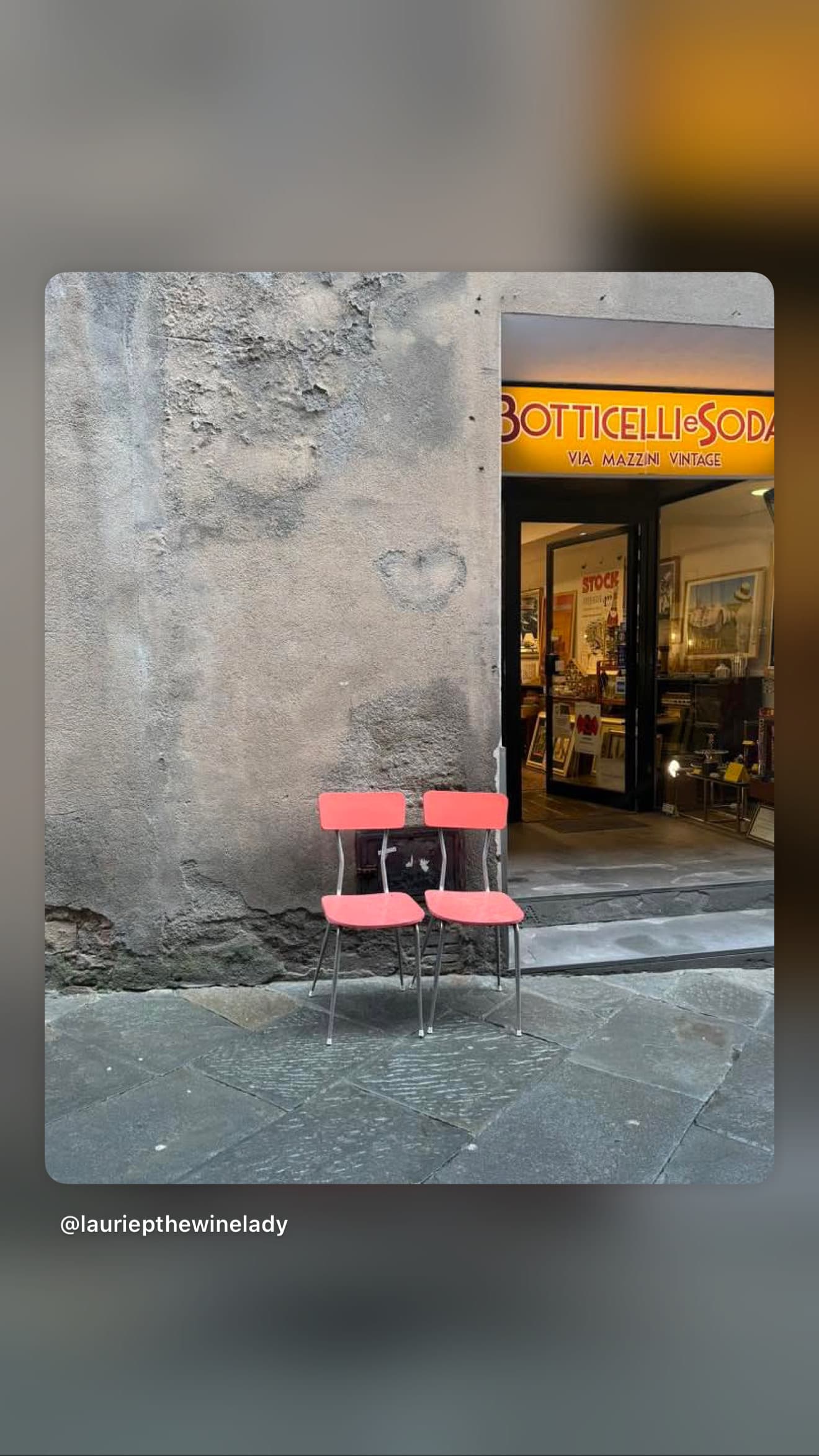 Two pink chairs on a stone street outside a vintage shop with a yellow sign.