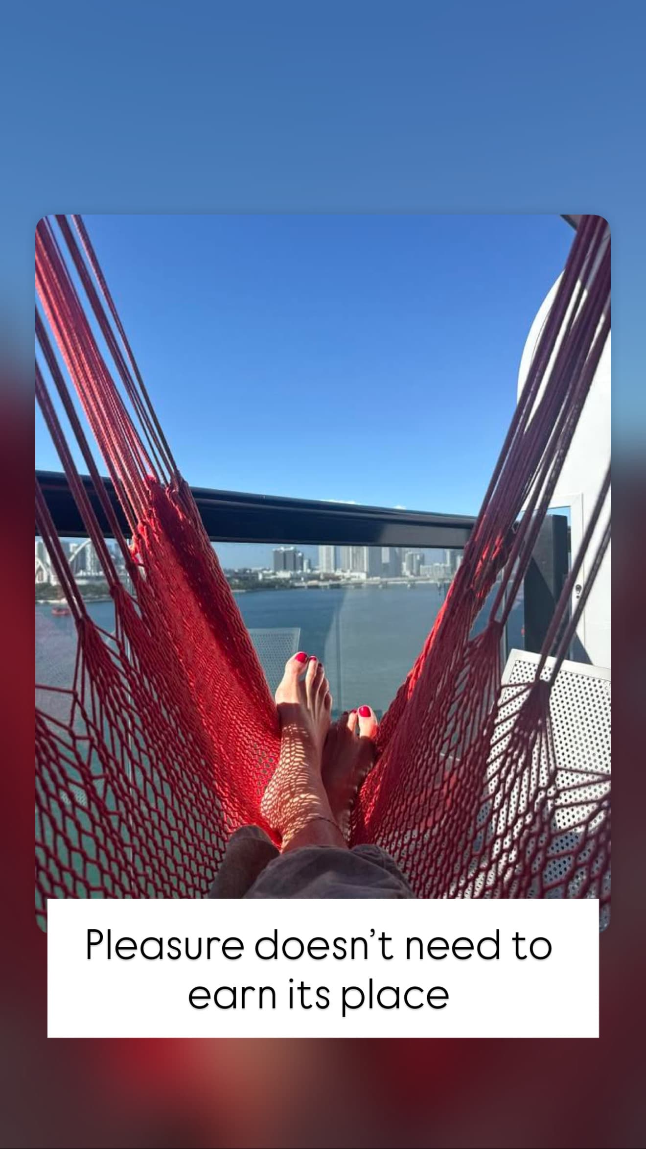 Feet with red polish in a red hammock overlooking a city skyline and blue water.