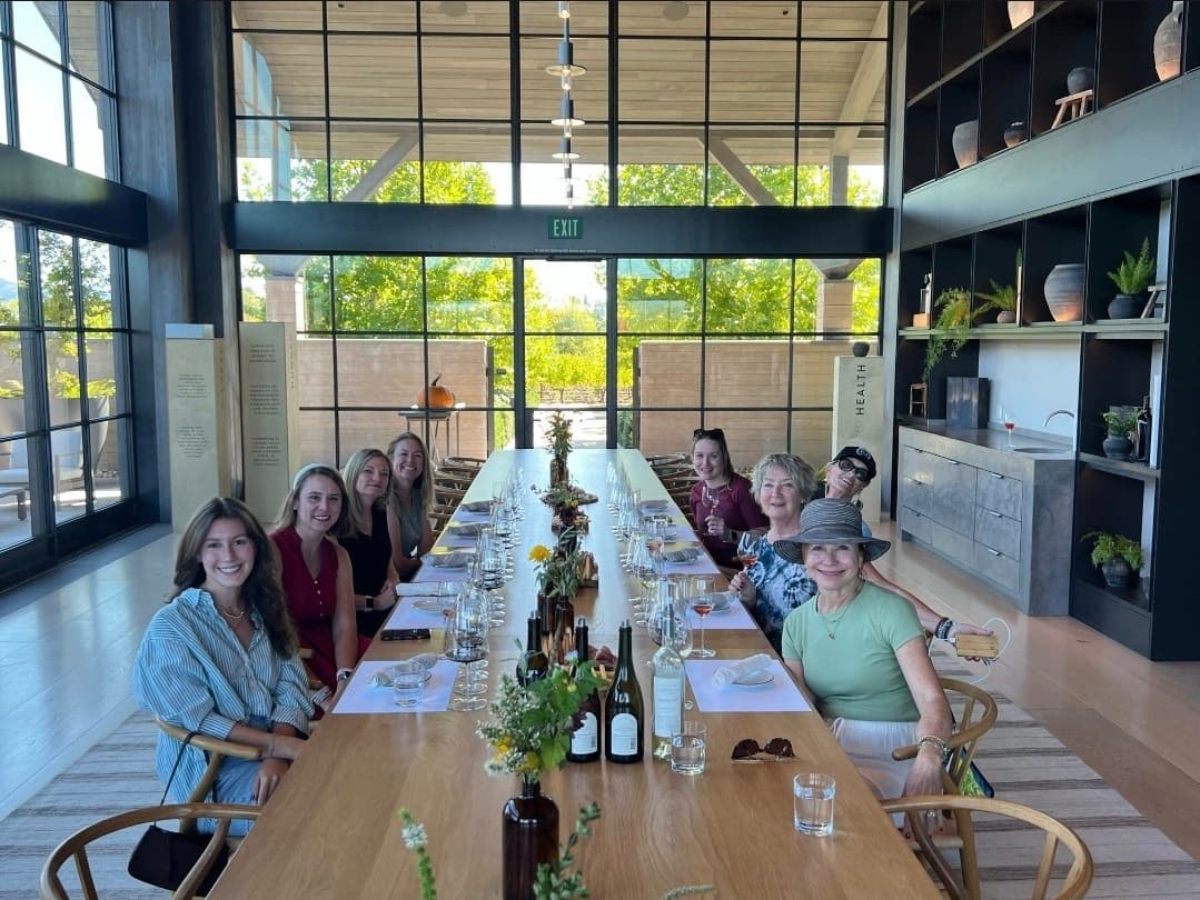 Women gathered at a long table for a wine tasting in a sunlit room.